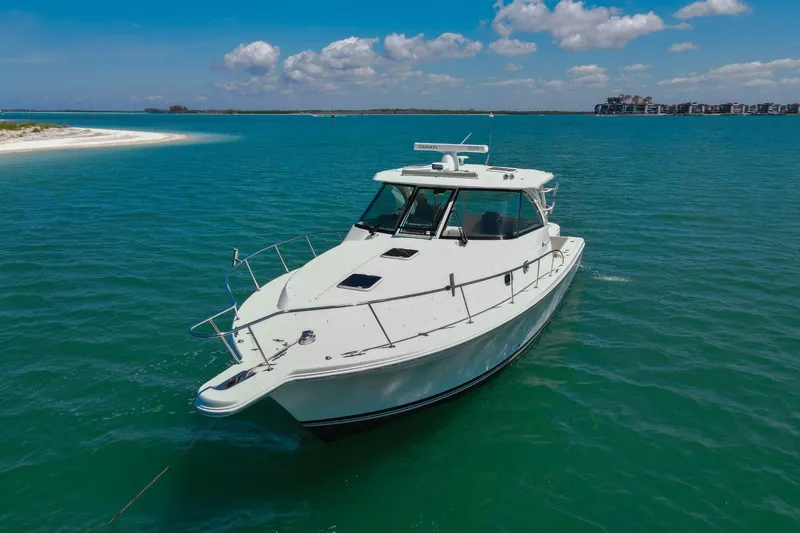 Slide: The Image of 2019 Pursuit OS 385 Offshore boat on clear blue water near a sandy shore. - 48