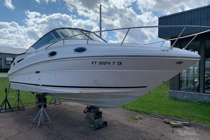 Slide: The Image of 2012 Sea Ray 240 Sundancer boat on stands, outdoors under a partly cloudy sky. - 2