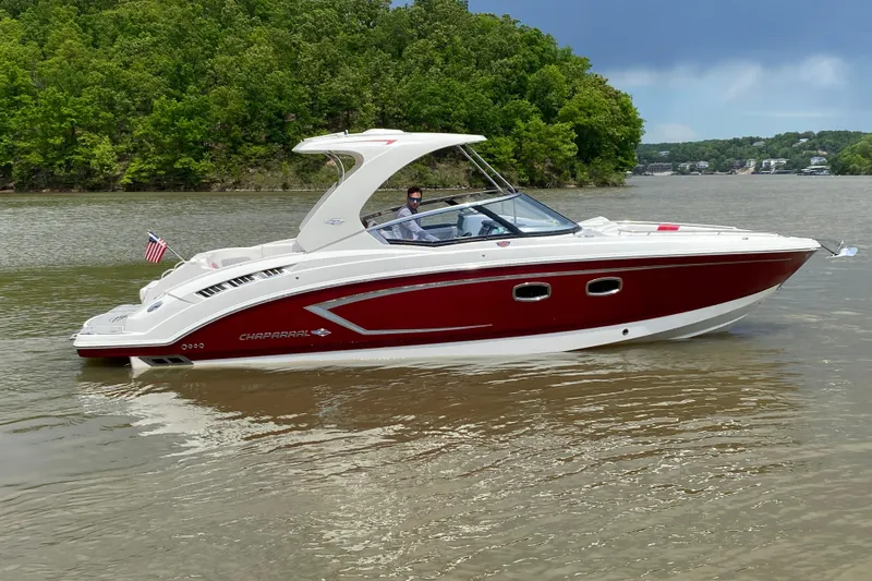 The Image of 2012 Chaparral 327 SSX boat cruising on a calm lake with lush green shoreline. - 1
