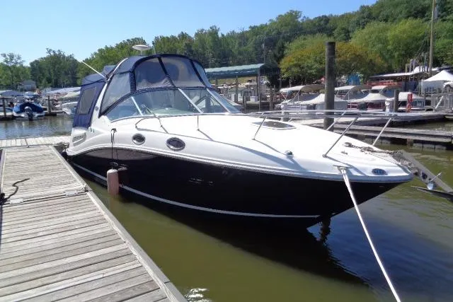 Slide: The Image of 2005 Sea Ray Sundancer 260 docked at a marina, featuring sleek design and canopy. - 2