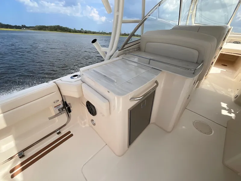 Slide: The Image of The image shows the deck of a 2027 Grady-White Freedom 285. It features a clean, bright surface with built-in fridge and seating. Water and a wooded shoreline are visible in the background. - 28