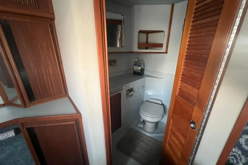 Slide: The Image of 1987 Sea Ray 410 Aft Cabin bathroom with wooden cabinets and compact toilet. - 21