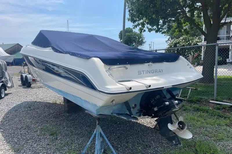 Slide: The Image of 2006 Stingray 230 LX boat with blue cover, parked on gravel near a fence. - 3