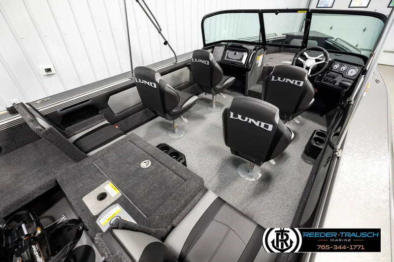 Slide: The Image of 2026 Lund 1875 Tyee boat interior with seating and dashboard, showcased in a showroom. - 11