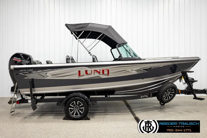 Slide: The Image of 2026 Lund 1875 Tyee boat with canopy on trailer, displayed indoors. - 4