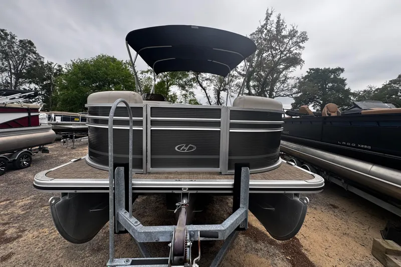 Slide: The Image of 2020 Harris Cruiser 210 pontoon boat with canopy, parked on a trailer, surrounded by trees. - 11