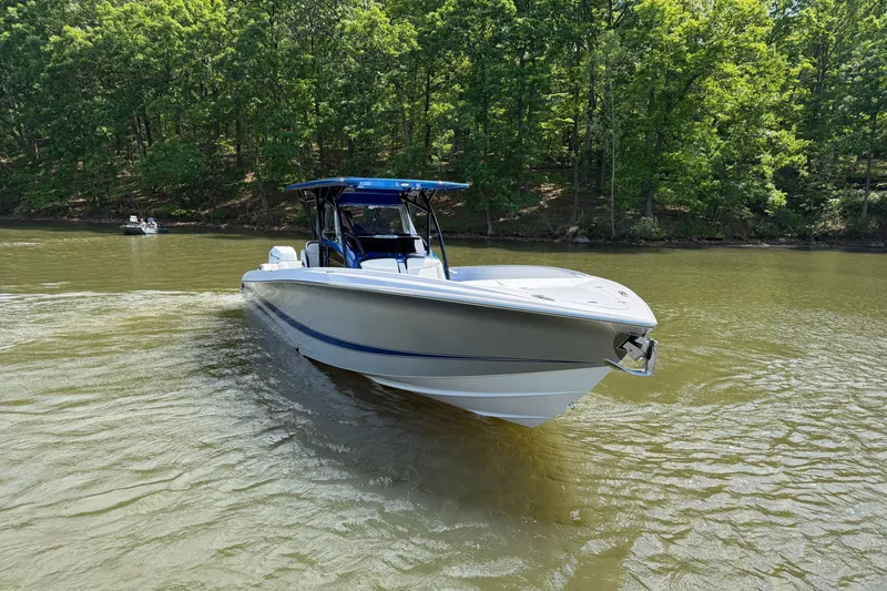 Slide: The Image of 2020 Nor-Tech 340 Sport Center Console boat cruising on a serene lake with lush green trees. - 2