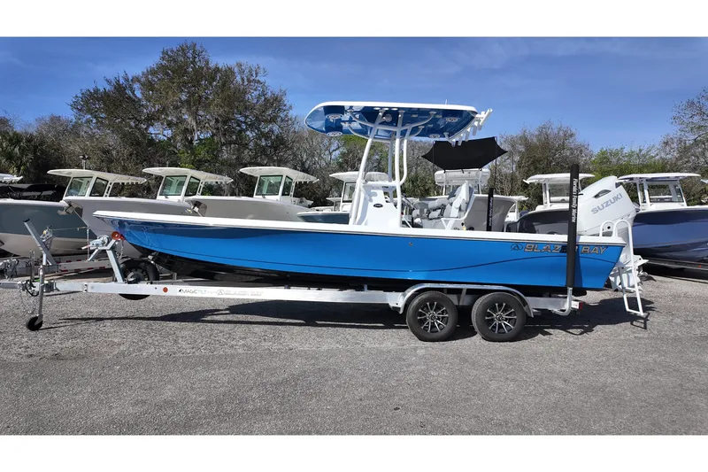 Slide: The Image of 2026 Blazer PureBay 2400 boat on trailer, blue hull, parked outdoors. - 2