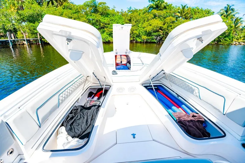Slide: The Image of 2018 Intrepid 327 Center Console boat with open storage compartments, docked by lush greenery. - 22