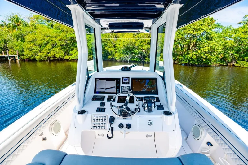Slide: The Image of 2018 Intrepid 327 Center Console boat cockpit with navigation screens, steering wheel, and lush waterway view. - 27