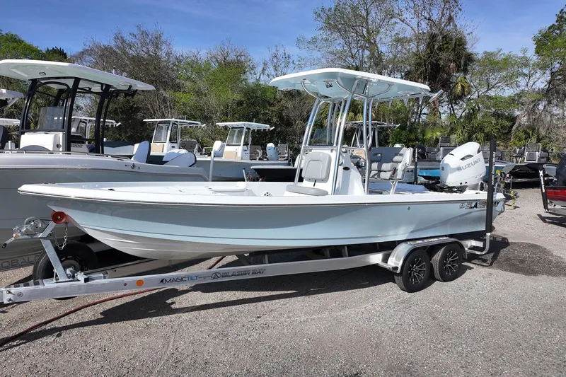 The Image of 2026 Blazer PureBay 2400 boat on trailer, parked outdoors, surrounded by trees and other boats. - 0