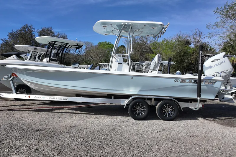 Slide: The Image of 2026 Blazer PureBay 2400 boat on trailer, featuring Suzuki engine, parked outdoors. - 2