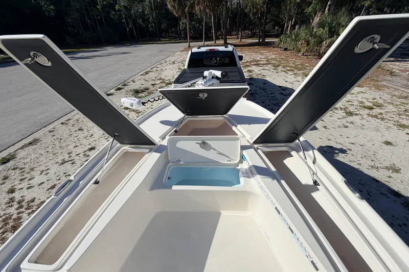 Slide: The Image of 2024 Key West 210 Bay Reef boat with open storage compartments, parked on a sandy roadside. - 46
