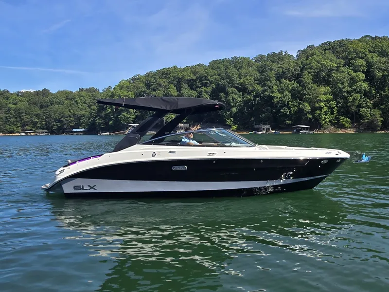 Slide: The Image of A 2026 Sea Ray SLX 260 Surf cruising on a calm lake with a wooded shoreline. - 30