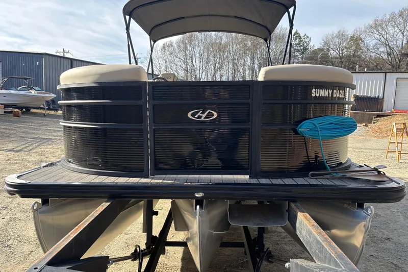 Slide: The Image of 2023 Harris Cruiser 230 pontoon boat in a yard, featuring black exterior and blue rope. - 11