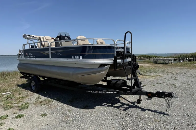 The Image of 2024 Sun Tracker Bass Buggy 18 DLX pontoon boat on trailer by a lakeside. - 0