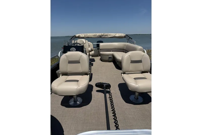Slide: The Image of 2024 Sun Tracker Bass Buggy 18 DLX pontoon boat with beige seating on a lake. - 2