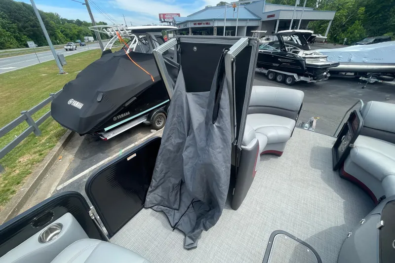 Slide: The Image of 2022 Manitou 23 Oasis pontoon boat interior with seating and privacy curtain, parked near Yamaha boat. - 13