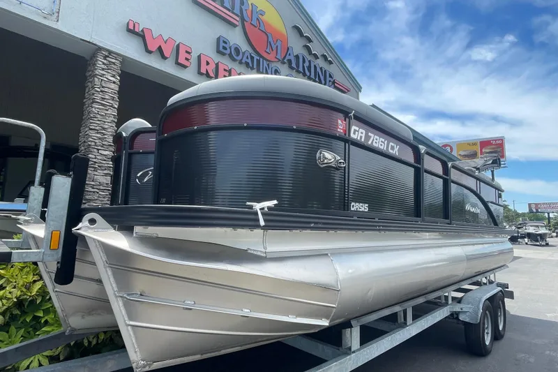 Slide: The Image of 2022 Manitou 23 Oasis pontoon boat on trailer at dealership under blue sky. - 2
