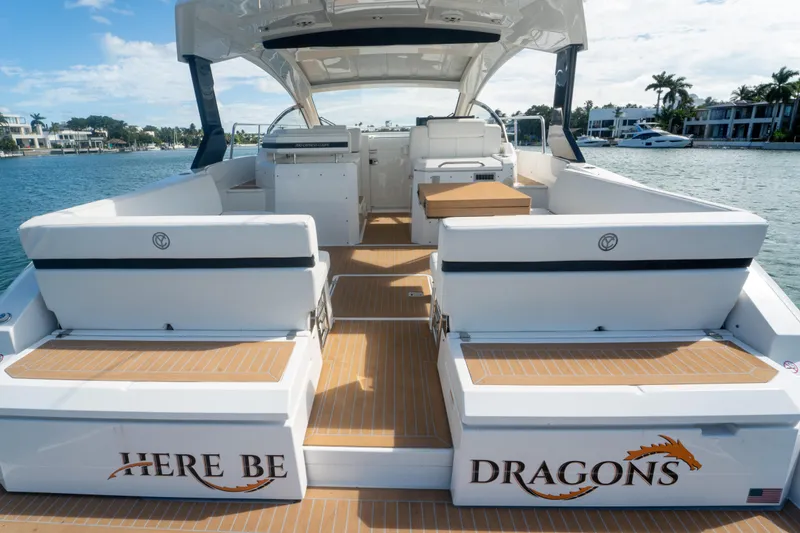 Slide: The Image of 2018 Cruisers Yachts 390 Express Coupe, spacious deck, "Here Be Dragons" text, waterfront view. - 28