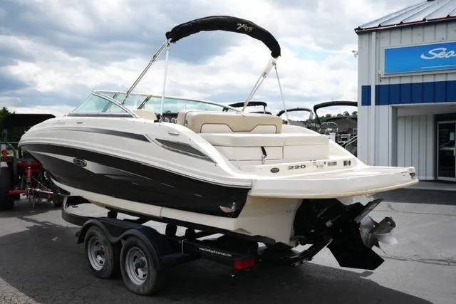 Slide: The Image of 2010 Sea Ray 220 Sundeck boat on trailer, parked outside dealership under cloudy sky. - 7