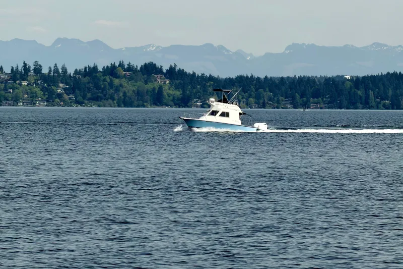 Slide: The Image of 1970 Bertram boat cruising on a serene lake with forested hills in the background. - 3