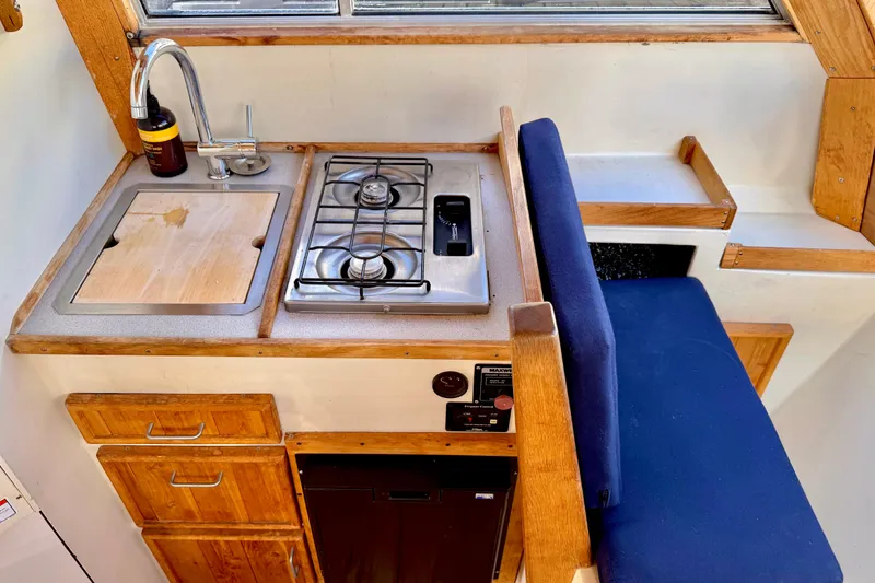 Slide: The Image of 1970 Bertram boat kitchen with stove, sink, wooden cabinets, and blue seating. - 6