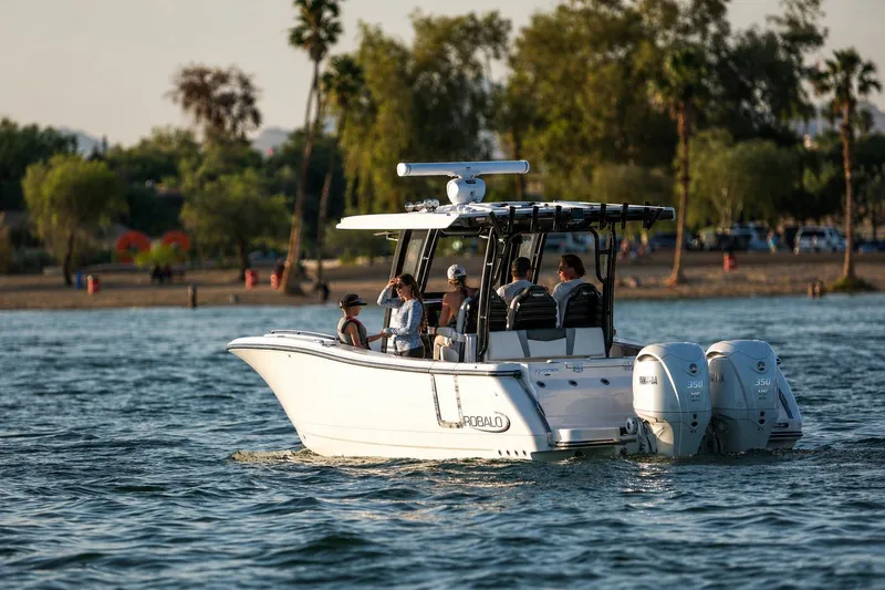 The Image of 2025 Robalo R300 Center Console boat cruising on a scenic lake with passengers. - 1