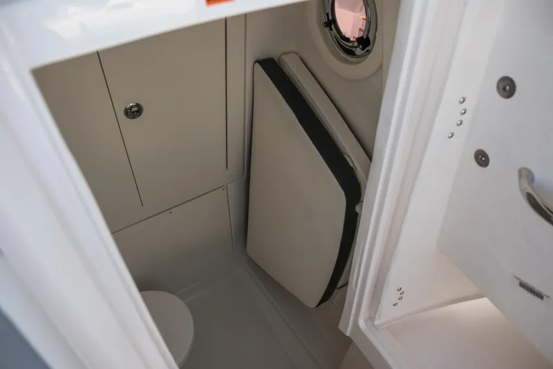 Slide: The Image of 2025 Robalo R300 Center Console boat interior with compact restroom and porthole. - 26
