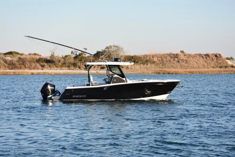 Slide: The Image of 2022 Blackfin 272 CC boat on calm water, with fishing rods and scenic background. - 5