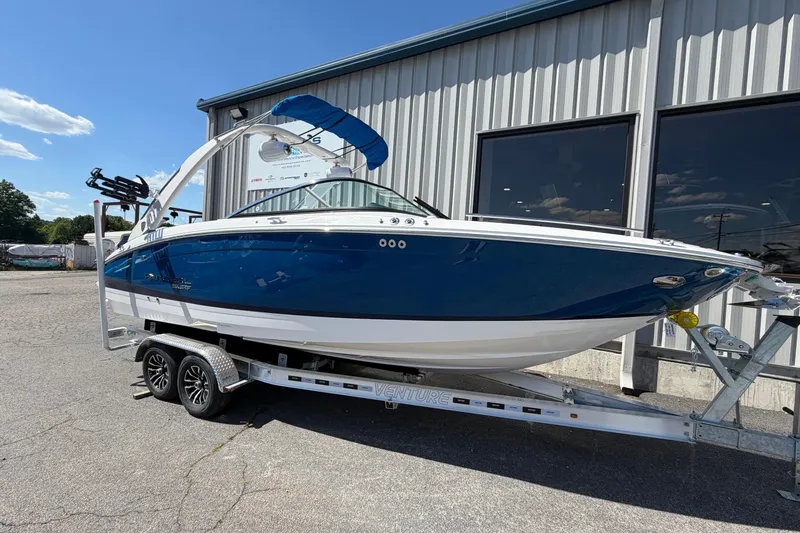 The Image of 2026 Regal LS6 Surf boat on trailer, blue and white exterior, parked outdoors. - 0