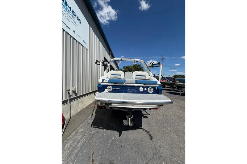 Slide: The Image of 2026 Regal LS6 Surf boat rear view, parked outdoors under a clear blue sky. - 2