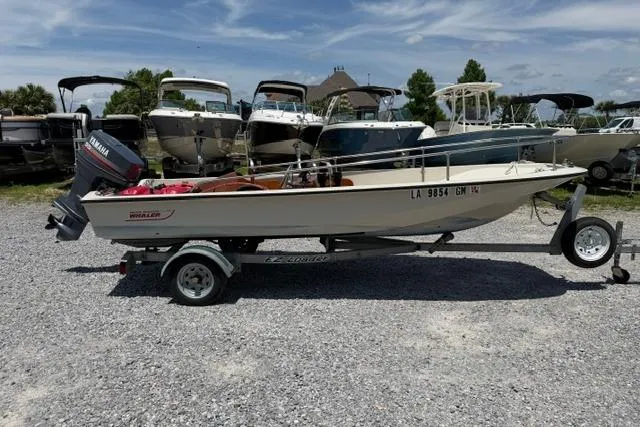 The Image of 1984 Boston Whaler 150 Sport boat on trailer, parked in a gravel lot with other boats. - 1