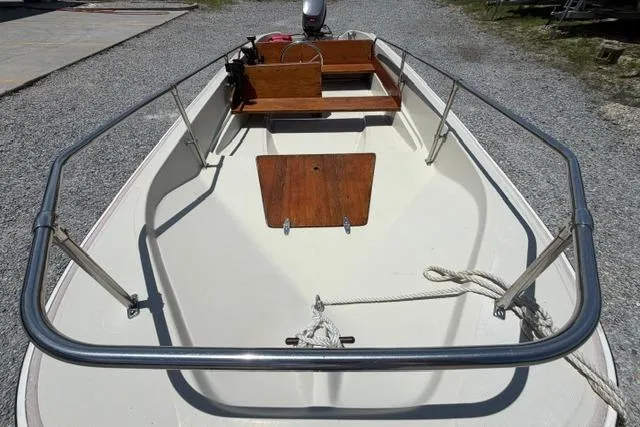 Slide: The Image of 1984 Boston Whaler 150 Sport boat with wooden seating and metal railings on gravel surface. - 8