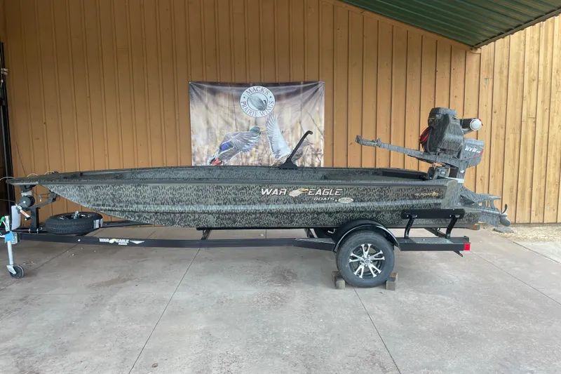Slide: The Image of 2026 War Eagle 750 Gladiator boat on trailer, displayed outdoors with wooden backdrop. - 22