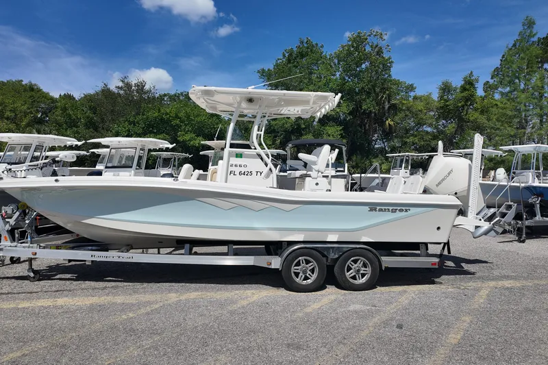 The Image of 2024 Ranger 2660 Bay boat on trailer, parked outdoors under clear blue sky. - 0