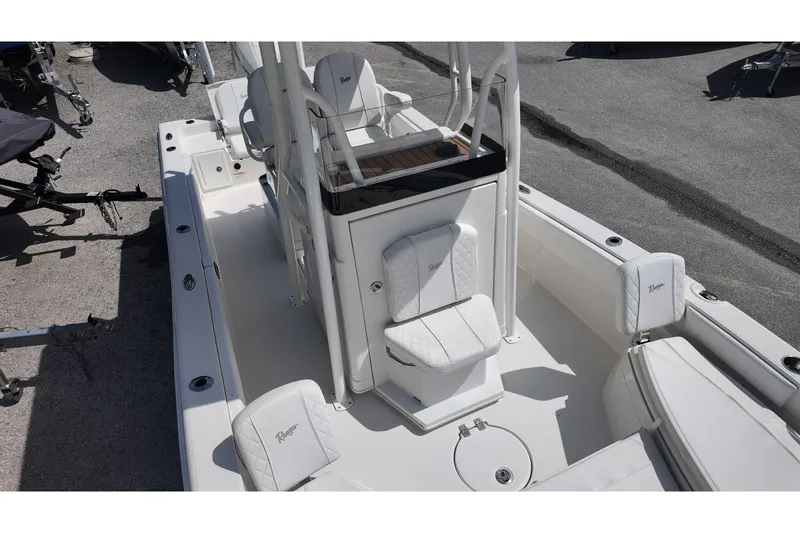 Slide: The Image of 2024 Ranger 2660 Bay boat interior with white seating and console, parked on pavement. - 11