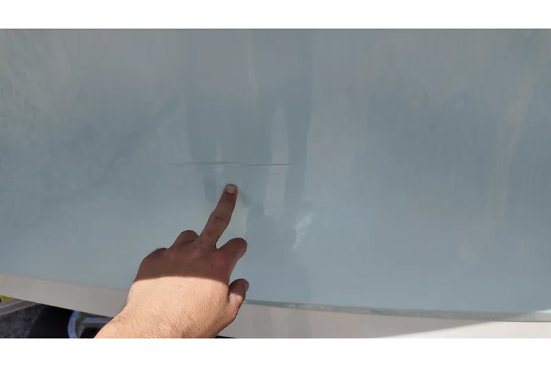 Slide: The Image of A hand pointing at a scratch on a 2024 Ranger 2660 Bay boat hull. - 21