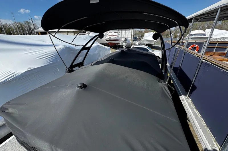 The Image of 2022 Bennington 24LX pontoon boat with black cover, docked alongside other boats. - 0