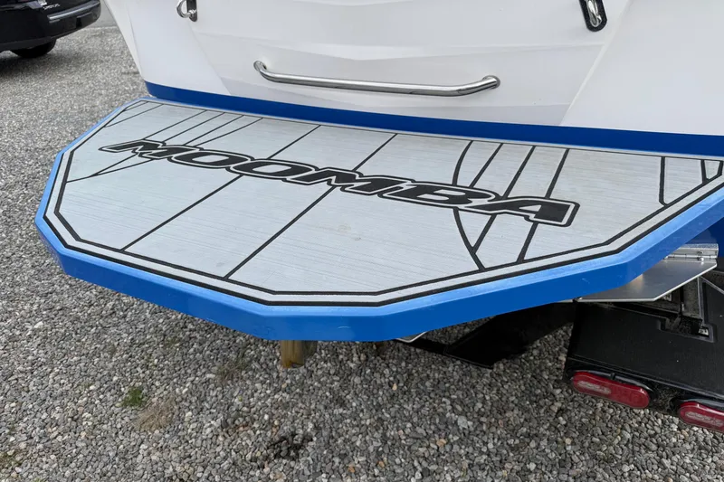 Slide: The Image of 2021 Moomba Kaiyen boat swim platform with logo, blue trim, on gravel surface. - 6