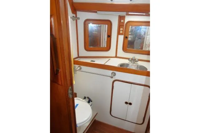 Slide: The Image of 1986 Tayana 52 Center Cockpit bathroom with wooden accents, sink, and porthole windows. - 22