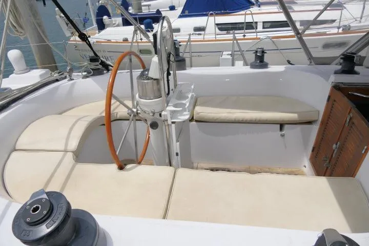 Slide: The Image of 1986 Tayana 52 Center Cockpit sailboat with wooden wheel and cushioned seating in marina. - 34