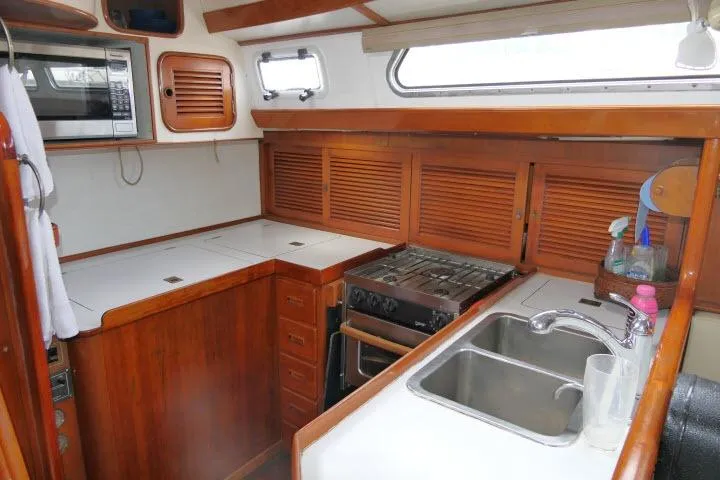 Slide: The Image of 1986 Tayana 52 Center Cockpit galley with wooden cabinetry, stove, microwave, and dual sink. - 9