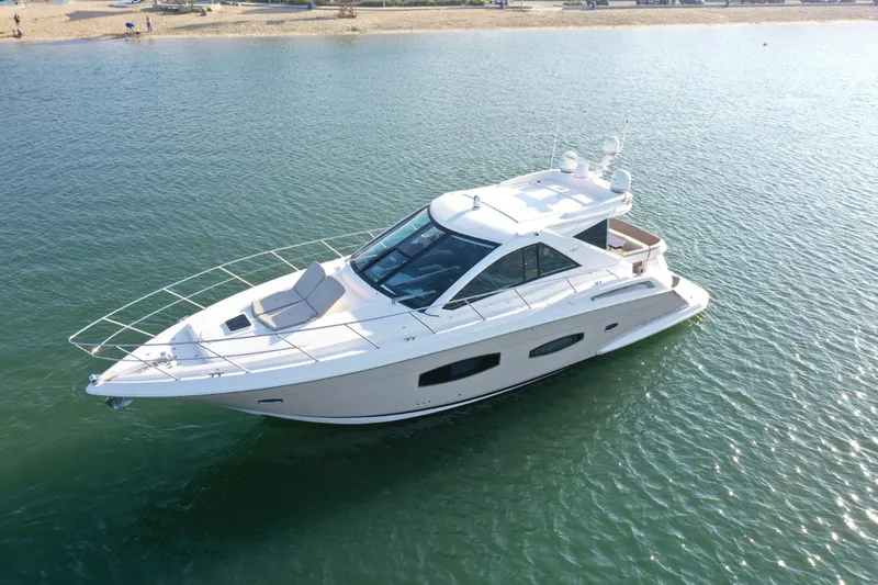The Image of 2015 Regal 53 Sport Coupe yacht cruising on calm waters near a sandy beach. - 1