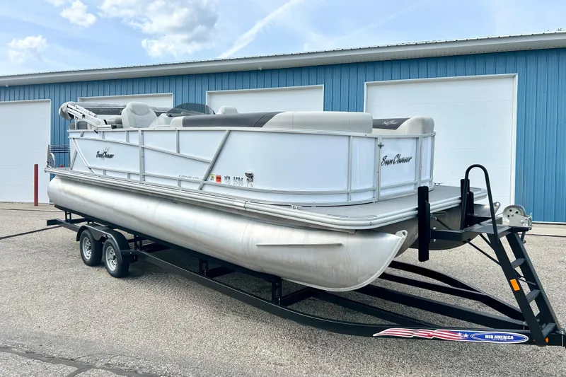 The Image of 2023 Sun Chaser Geneva pontoon boat on trailer, parked outside blue warehouse. - 1