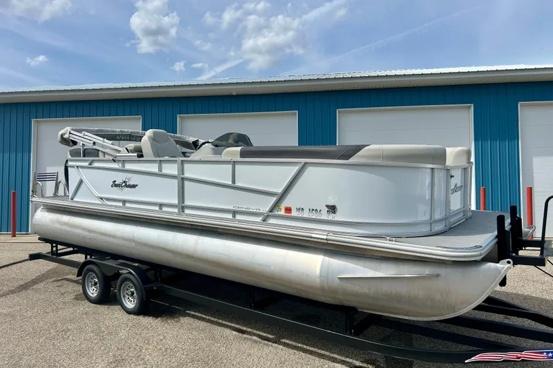 Slide: The Image of 2023 Sun Chaser Geneva pontoon boat on trailer, parked outside blue building. - 14