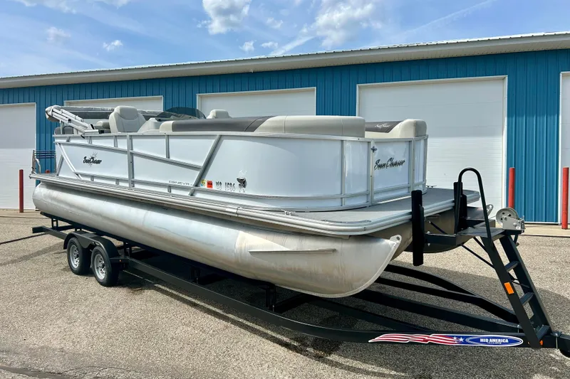 Slide: The Image of 2023 Sun Chaser Geneva pontoon boat on trailer, parked outside blue warehouse. - 15