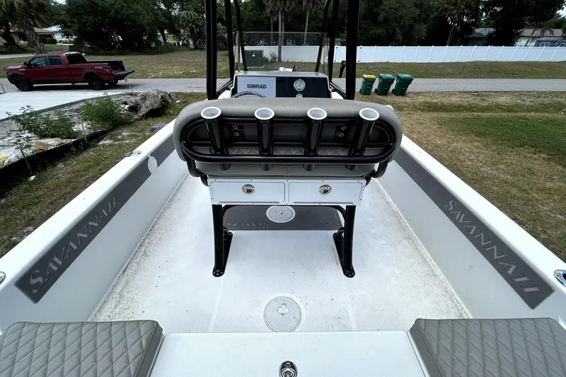 Slide: The Image of 2025 Savannah 210X boat interior with seating and rod holders, parked outdoors. - 13