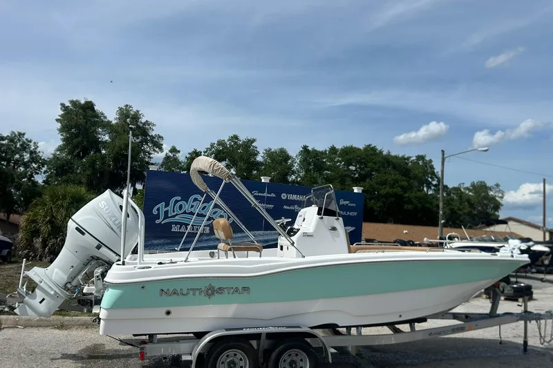 The Image of 2024 NauticStar 211 Hybrid boat on trailer, parked outdoors under a clear sky. - 1