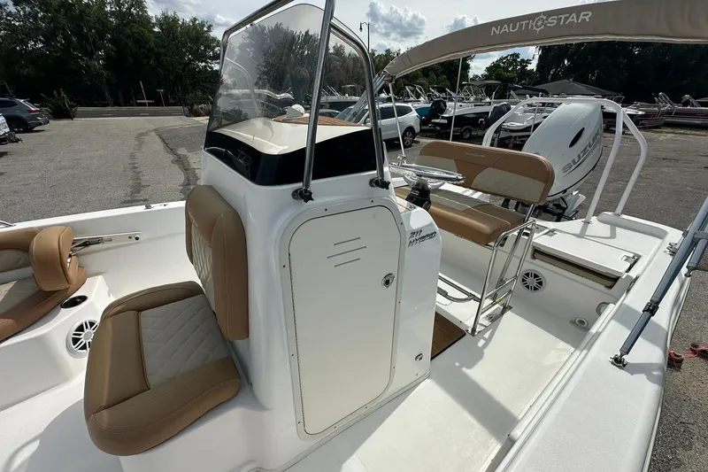 Slide: The Image of 2024 NauticStar 211 Hybrid boat interior with tan seating and console, parked outdoors. - 17